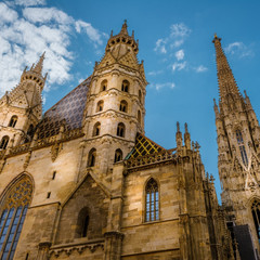 © Westlightart Der Stephansdom in Wien mit seinen gotischen Türmen und dem bunt gefliesten Dach vor blauem Himmel mit ein paar Wolken.