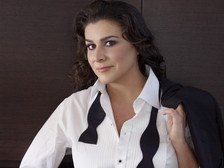 © Uli Weber Cecilia Bartoli im weißen Hemd mit offenem Smokinghemd und schwarzer Fliege, die Jacke lässig über die Schulter gelegt, vor dunklem Hintergrund.