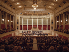 © Markenfotografie Großes Sinfoniekonzert in einem prunkvollen historischen Konzertsaal mit Orchester auf der Bühne und voll besetztem Publikum.